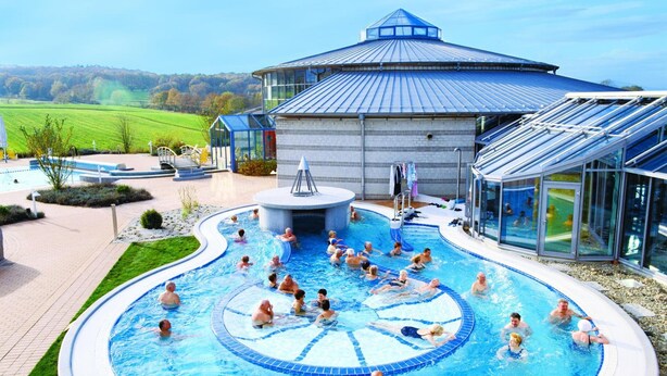 Une grande piscine extérieure de forme circulaire, entourée d’une pelouse et bordée d’un bâtiment dont le toit est bleu.