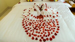 Una cama con un arreglo de pétalos de rosa en forma de corazón y dos cisnes hechos con toallas.