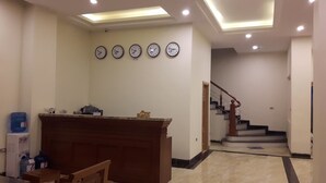 Un área de recepción con mostrador, cuatro relojes de pared, una escalera y un dispensador de agua.