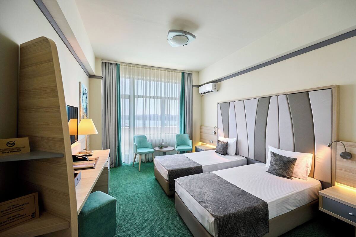 Ein Hotelzimmer mit zwei Betten, einem Schreibtisch, einem Stuhl und einem kleinen Tisch.