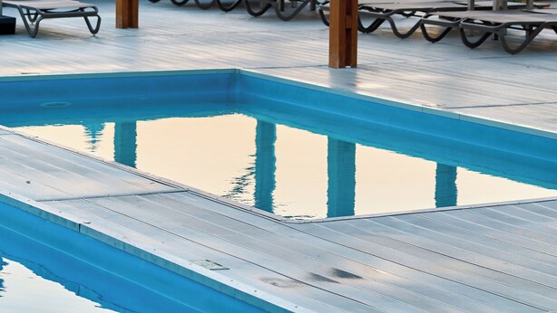 Une terrasse en bois, dotée de chaises longues et de parasols, qui offre une vue sur une étendue d’eau calme.