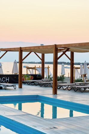 Eine Holzterrasse mit Liegestühlen und Sonnenschirmen mit Blick auf ruhiges Wasser.