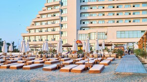 Un hôtel à plusieurs étages, doté d’espaces extérieurs aménagés avec des parasols, et un ciel dégagé.