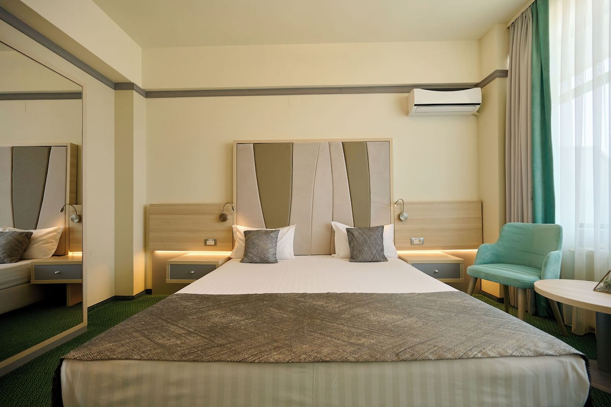Ein Hotelzimmer mit einem großen Bett, zwei Nachttischen, einem kleinen Tisch, einem Sessel und einer Klimaanlage.