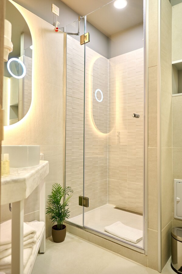 Un baño moderno con cabina de ducha de vidrio, un lavabo blanco y una planta en maceta.