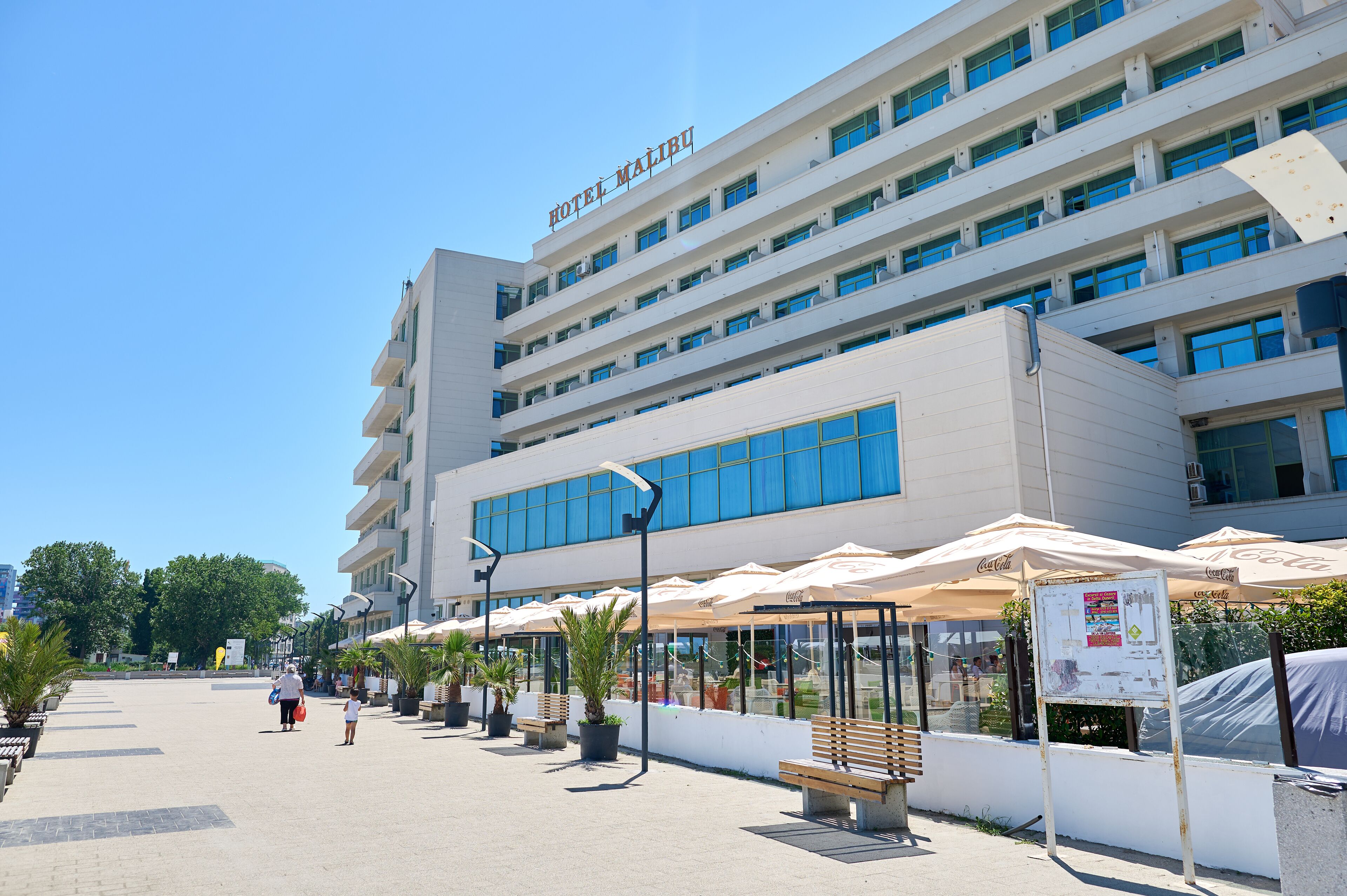 A hotel with multiple floors, outdoor seating areas with umbrellas, and a clear sky.