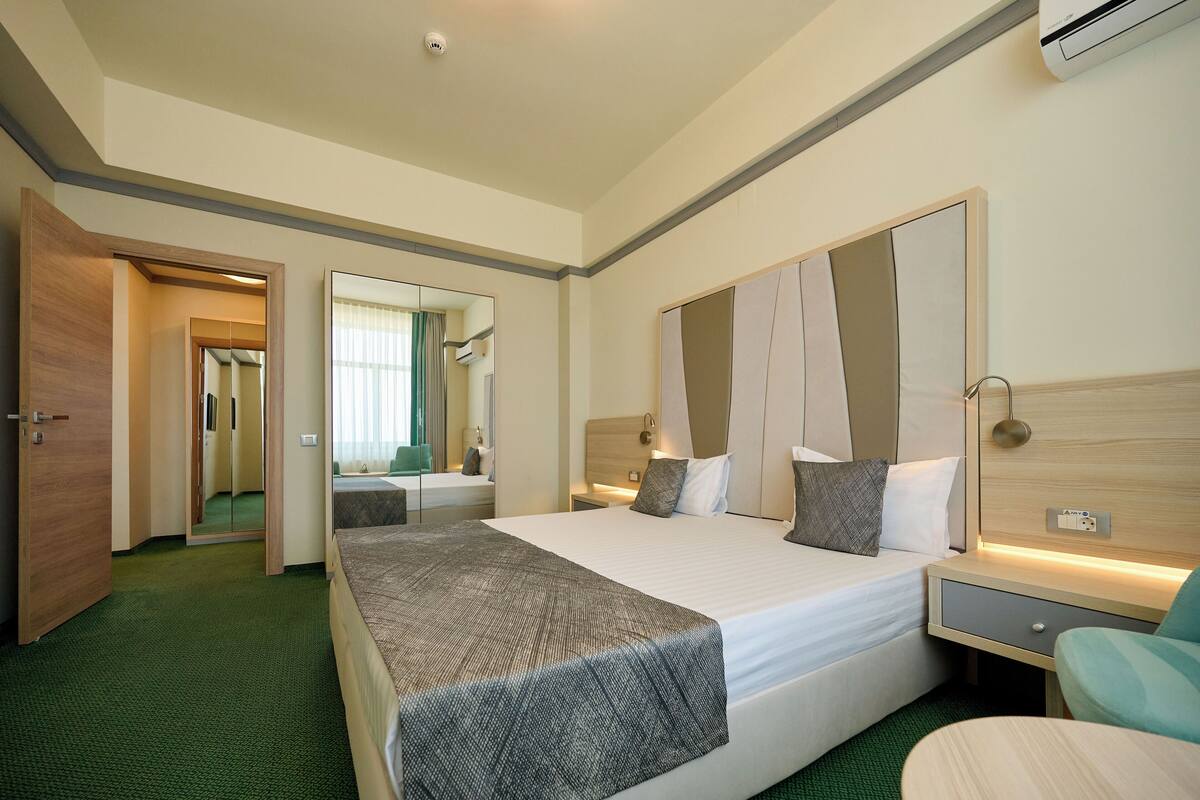 Ein Hotelzimmer mit einem großen Bett, Nachttischen, einem Spiegel und einem grünen Teppich.