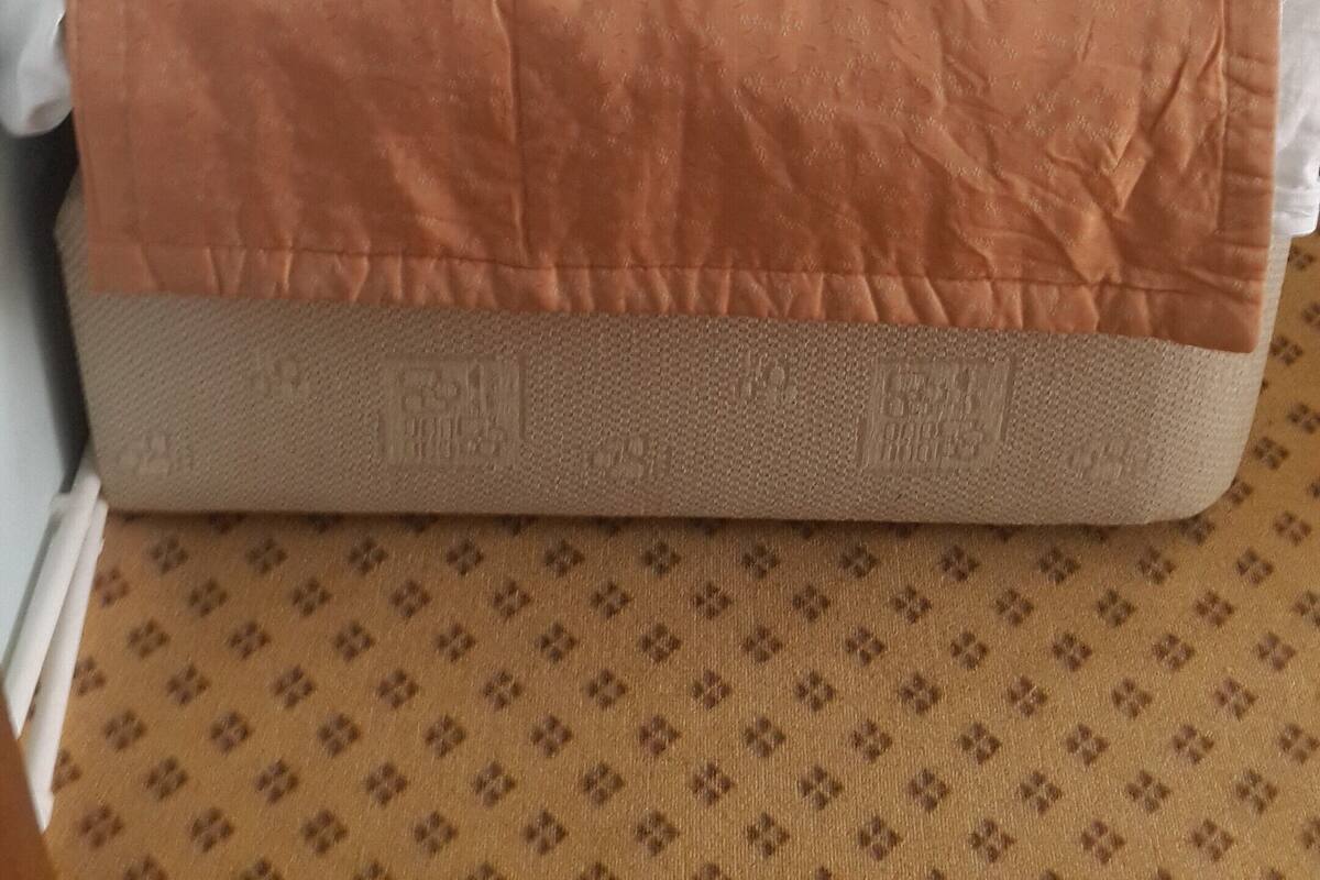 A bed with a brown mattress and a purple pillow in a room with light blue walls and a patterned carpet.