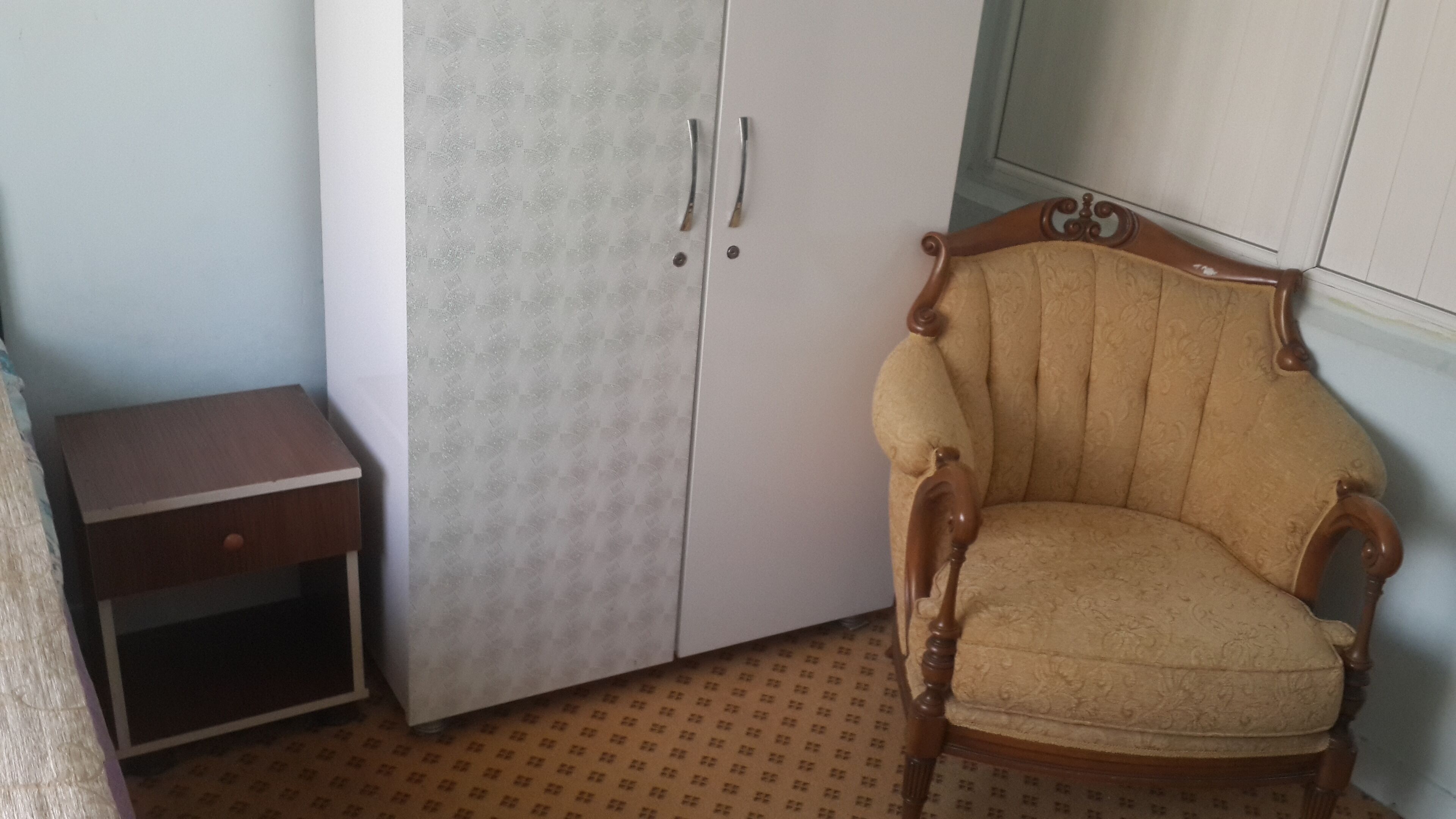 A room with a wardrobe, a wooden chair, and a small wooden table.