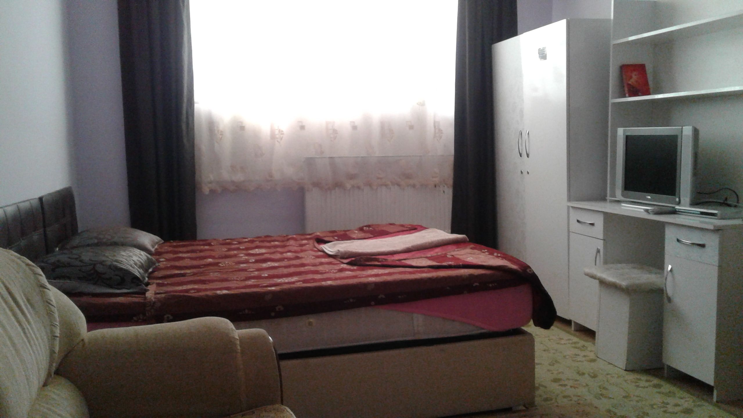 A bedroom with a bed, a desk with a TV, a wardrobe, and a chair.