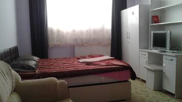 Un dormitorio con cama, escritorio con televisor, armario y una silla.