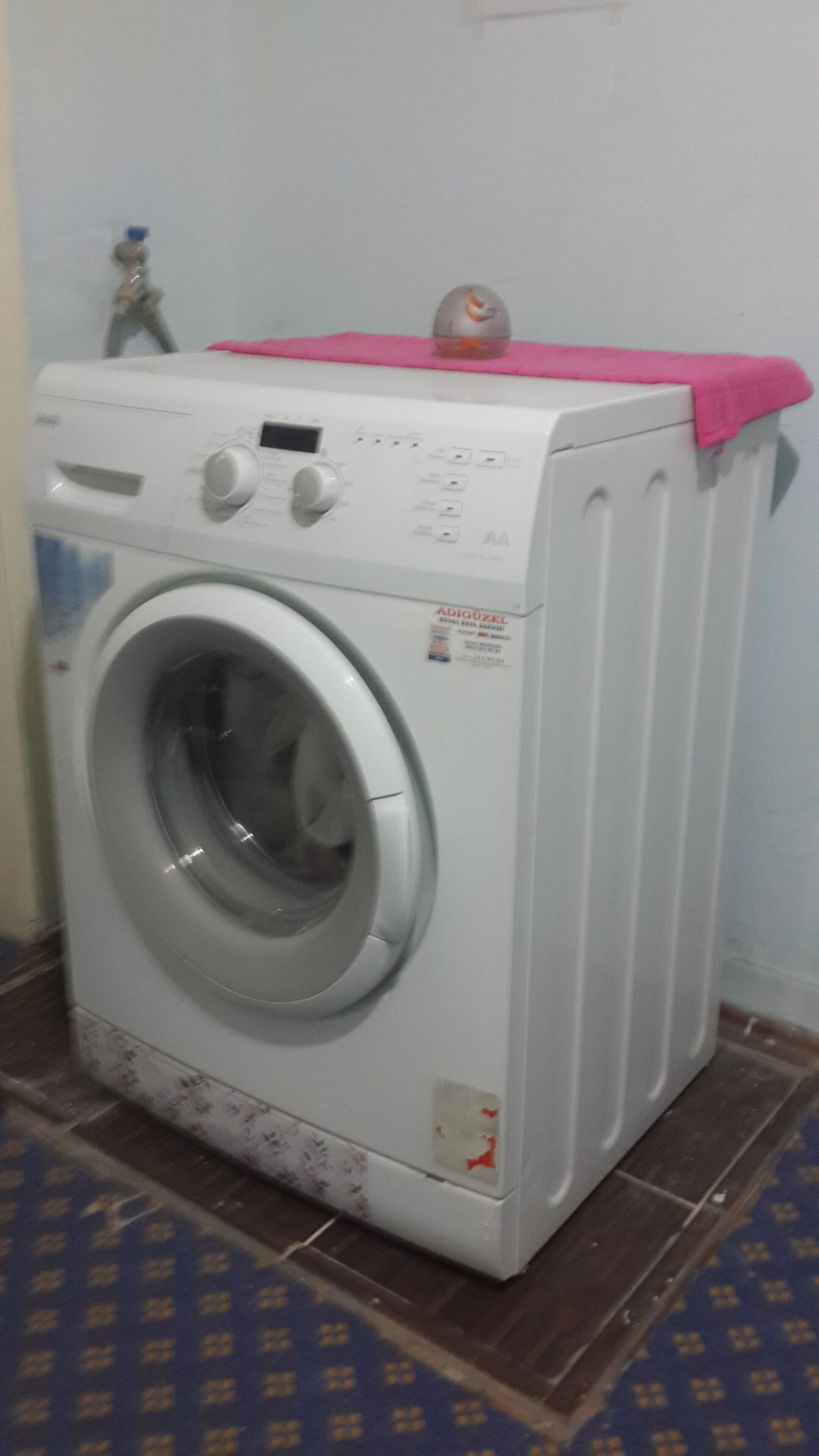 A front-loading washing machine with a pink cloth on top, placed on a patterned floor.