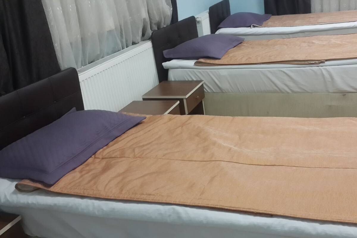 A hotel room with two beds, each with a headboard, a bedside table, and a window with curtains.