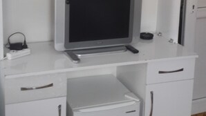 Un escritorio blanco con televisor, un refrigerador pequeño y un estante arriba.