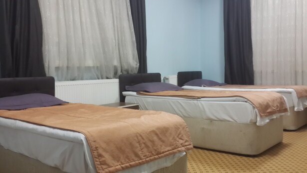 Una habitación de hotel con dos camas individuales, un sofá, un radiador y una ventana con cortinas traslúcidas.