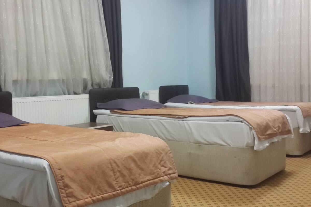 A hotel room with two single beds, a sofa, a radiator, and a window with sheer curtains.