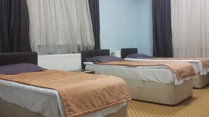A hotel room with two single beds, a sofa, a radiator, and a window with sheer curtains. - Esin Pansiyon (Tokat)