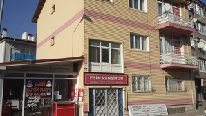 Un edificio con un letrero rojo que dice "ESIN PANSIYON" y un escaparate visible con un letrero que indica "ESIN BUTIK KAFE".