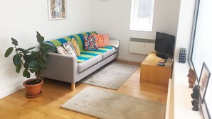 Un salon avec un canapé, un téléviseur, une plante et une affiche accrochée au mur.