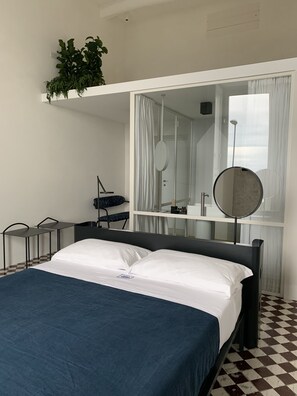 Quarto de hotel com cama, escrivaninha, cadeira, espelho e planta em vaso.