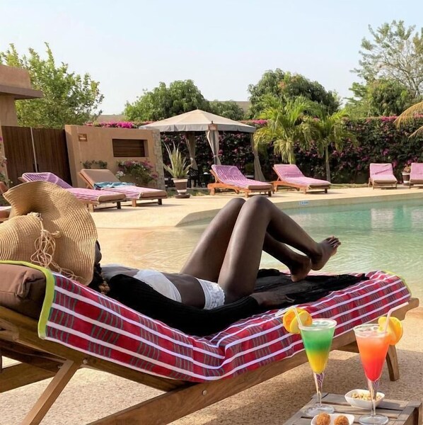 Un espace aménagé au bord de la piscine, avec des chaises longues, une piscine et une personne allongée sur une chaise.