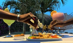 A table with food and drinks, palm trees, and a clear sky in the background. - Hôtel La Belle Etoile & SPA (Mbour)
