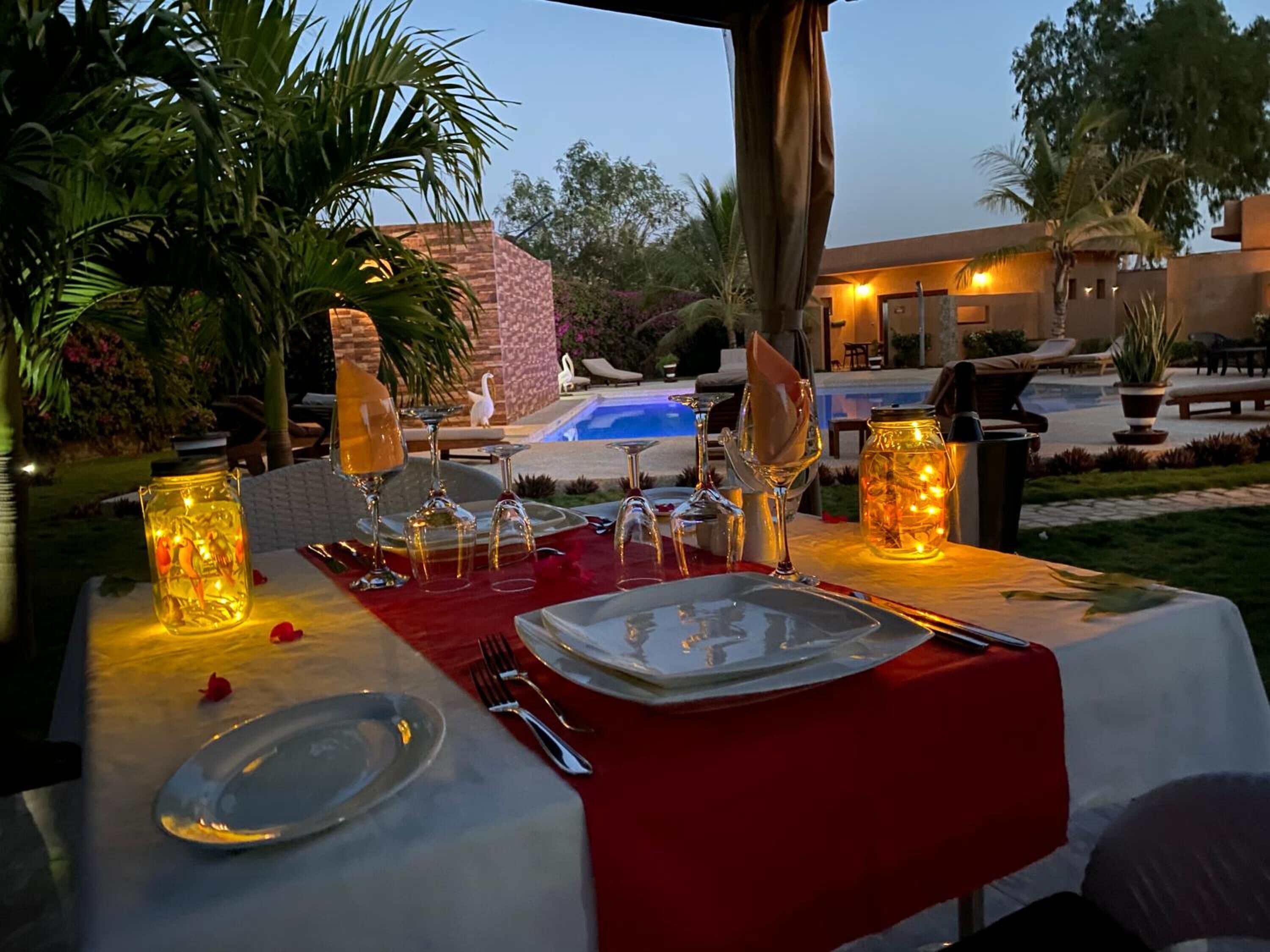 Un montaje para comer al aire libre con mantel rojo, varias copas de vino y un tarro decorativo con luces.