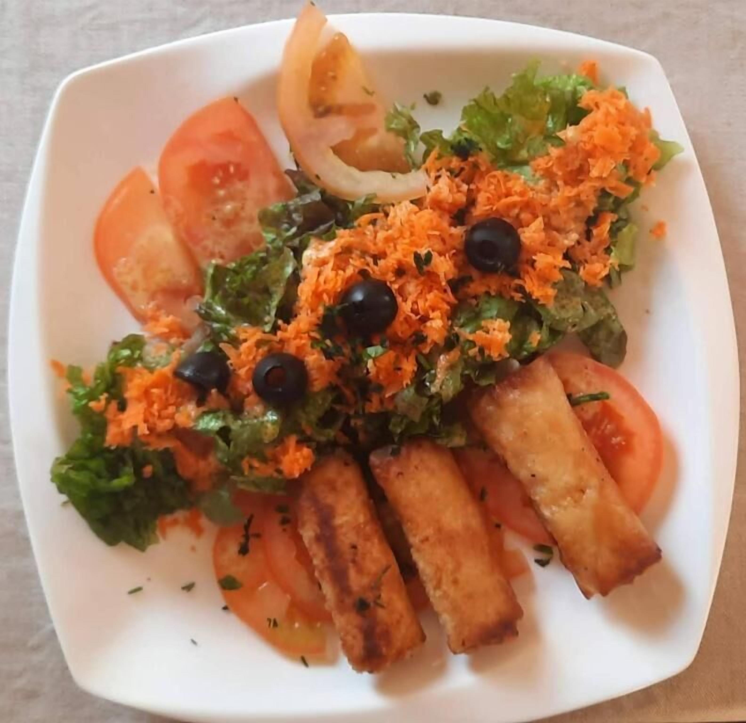 A white plate with a salad consisting of lettuce, tomatoes, black olives, and shredded carrots.
