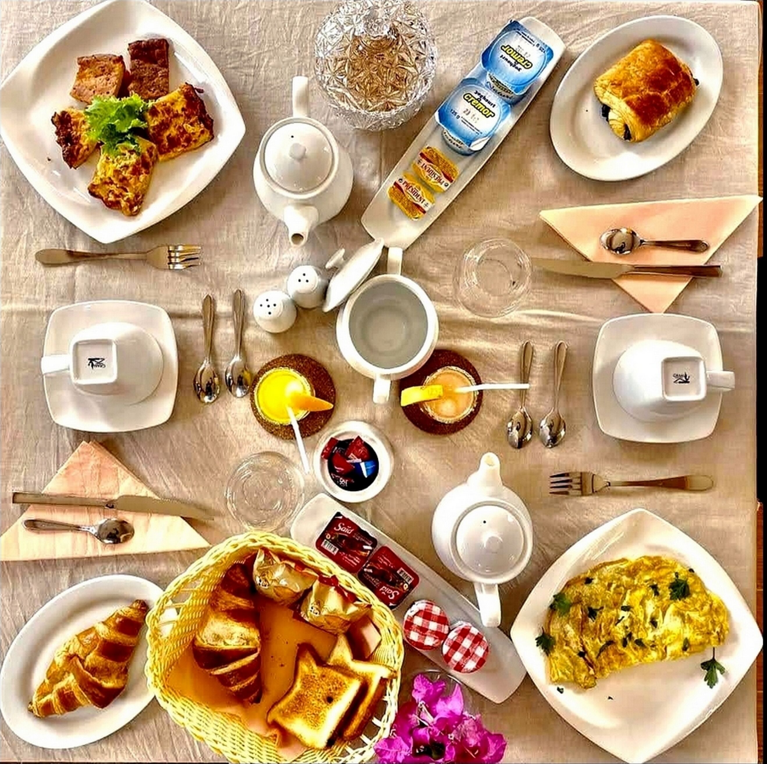 Une table en bois dressée pour le petit-déjeuner, avec divers aliments, ustensiles et une théière.