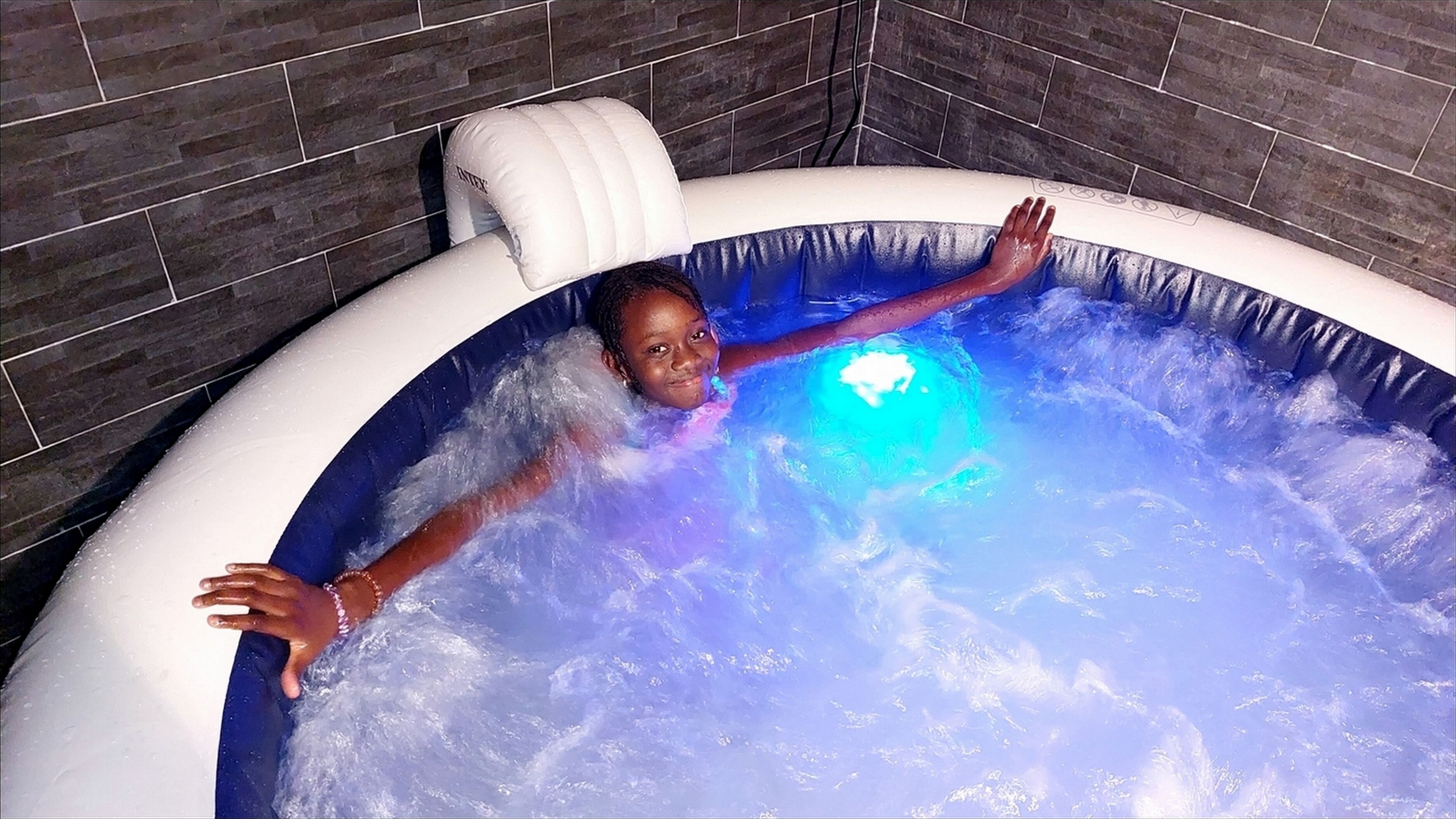 A child in a hot tub with a blue light, surrounded by water.
