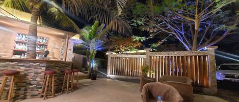 A bar area with stools, a stone wall, and a wooden fence.