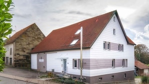 A two-story house with a red-tiled roof, a garage, and a small front yard with a bench.