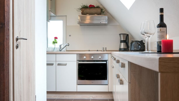 A modern kitchen with white cabinets, a built-in oven, and a skylight.