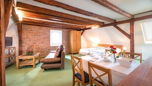 A cozy room with a brick wall, wooden beams, a bed, a table with chairs, and a small table with a plant.