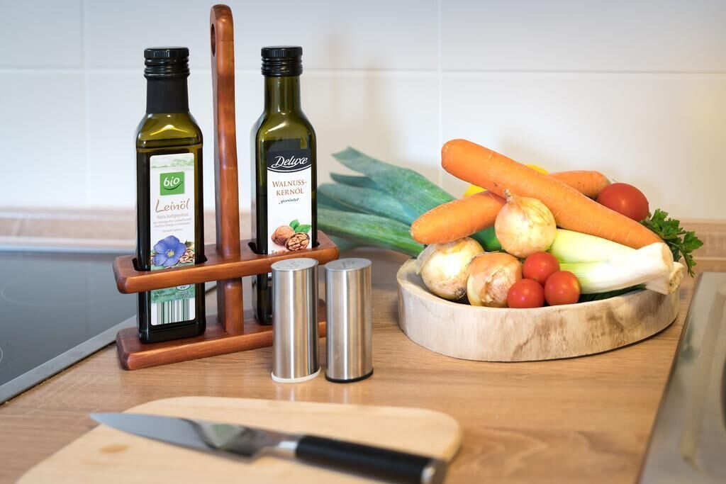 A kitchen counter with two bottles of oil, a wooden cutting board with vegetables, and a knife.