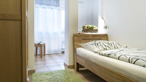 A bedroom with a wooden bed, a bedside table with a plant, and a window with sheer curtains.