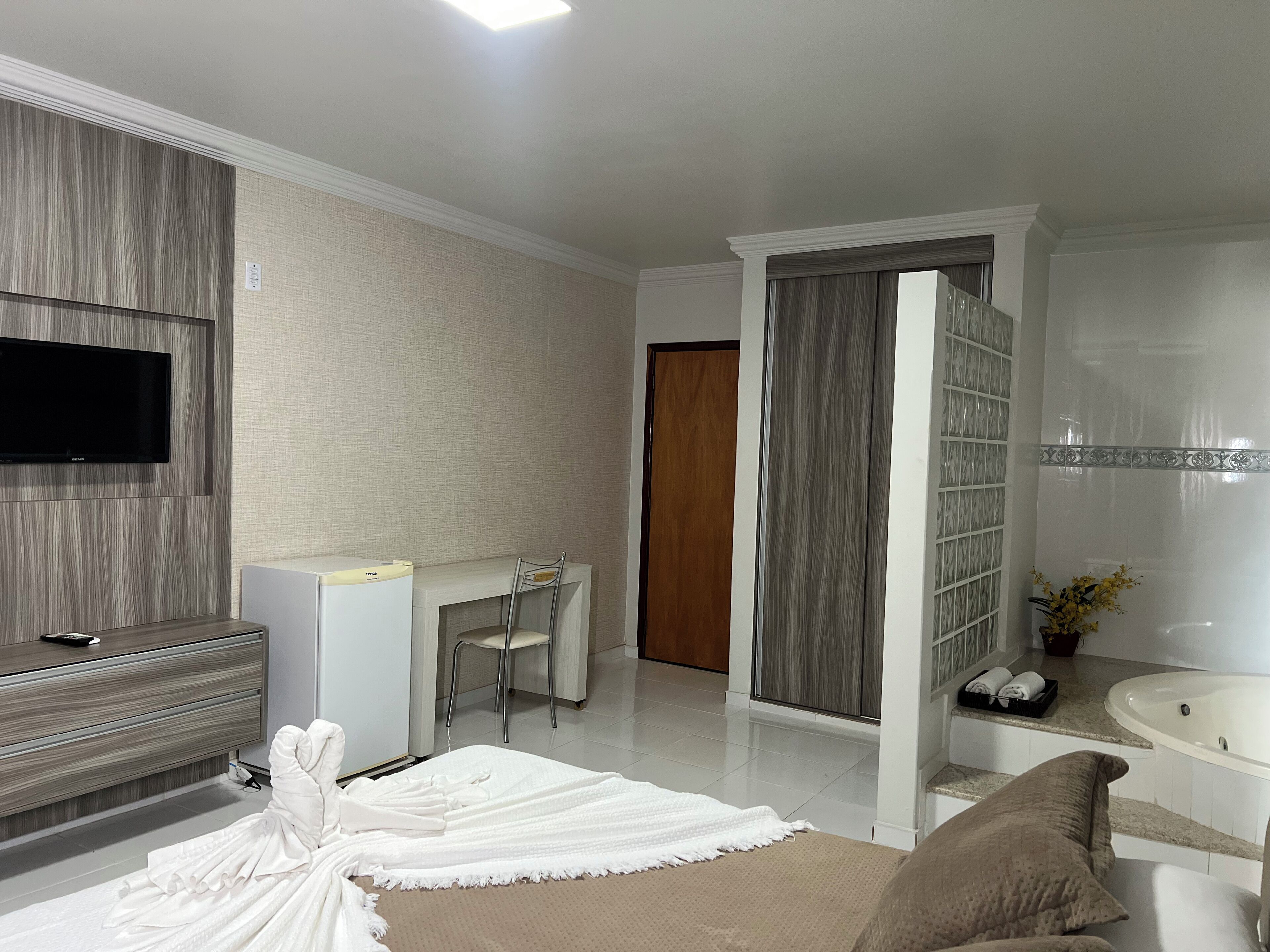 Habitación de hotel con televisión de pantalla plana, escritorio, silla, estantería, bañera y bata blanca.