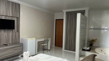 Habitación de hotel con televisión de pantalla plana, escritorio, silla, estantería, bañera y bata blanca.