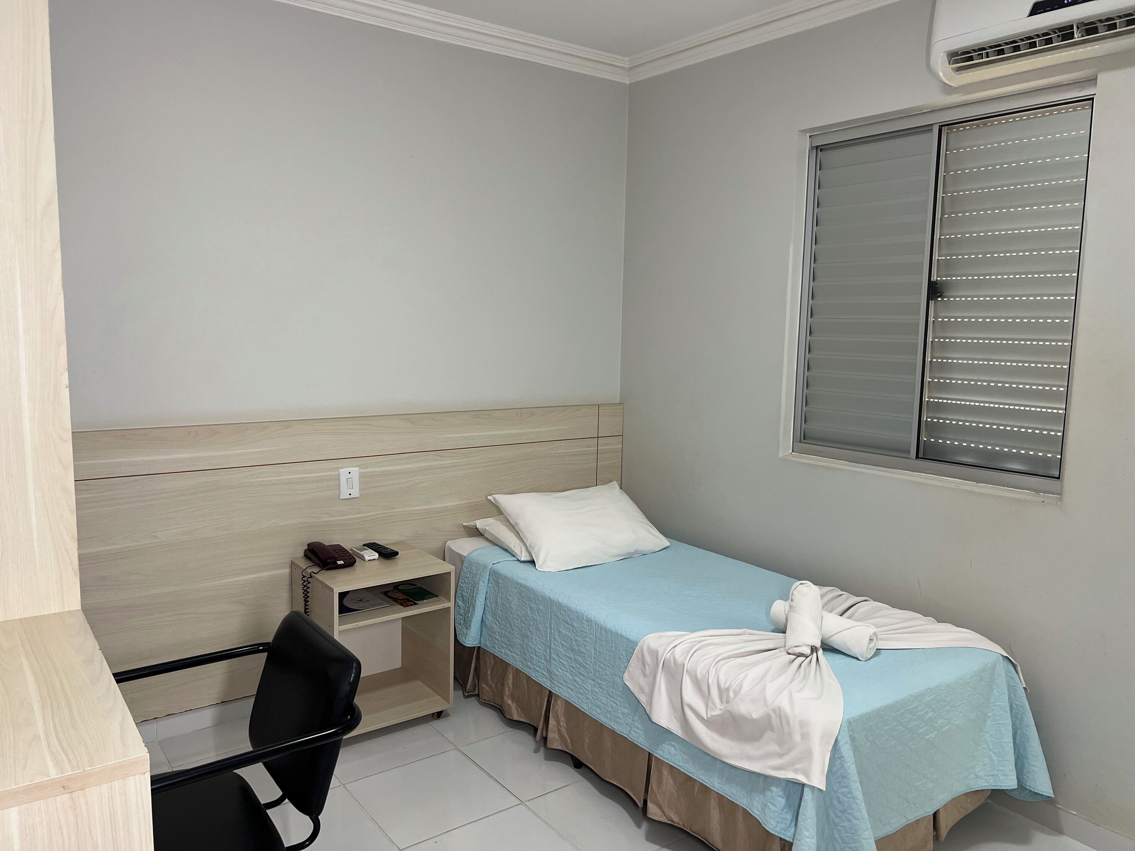 A small, neatly arranged room with a single bed, a desk, and a chair.