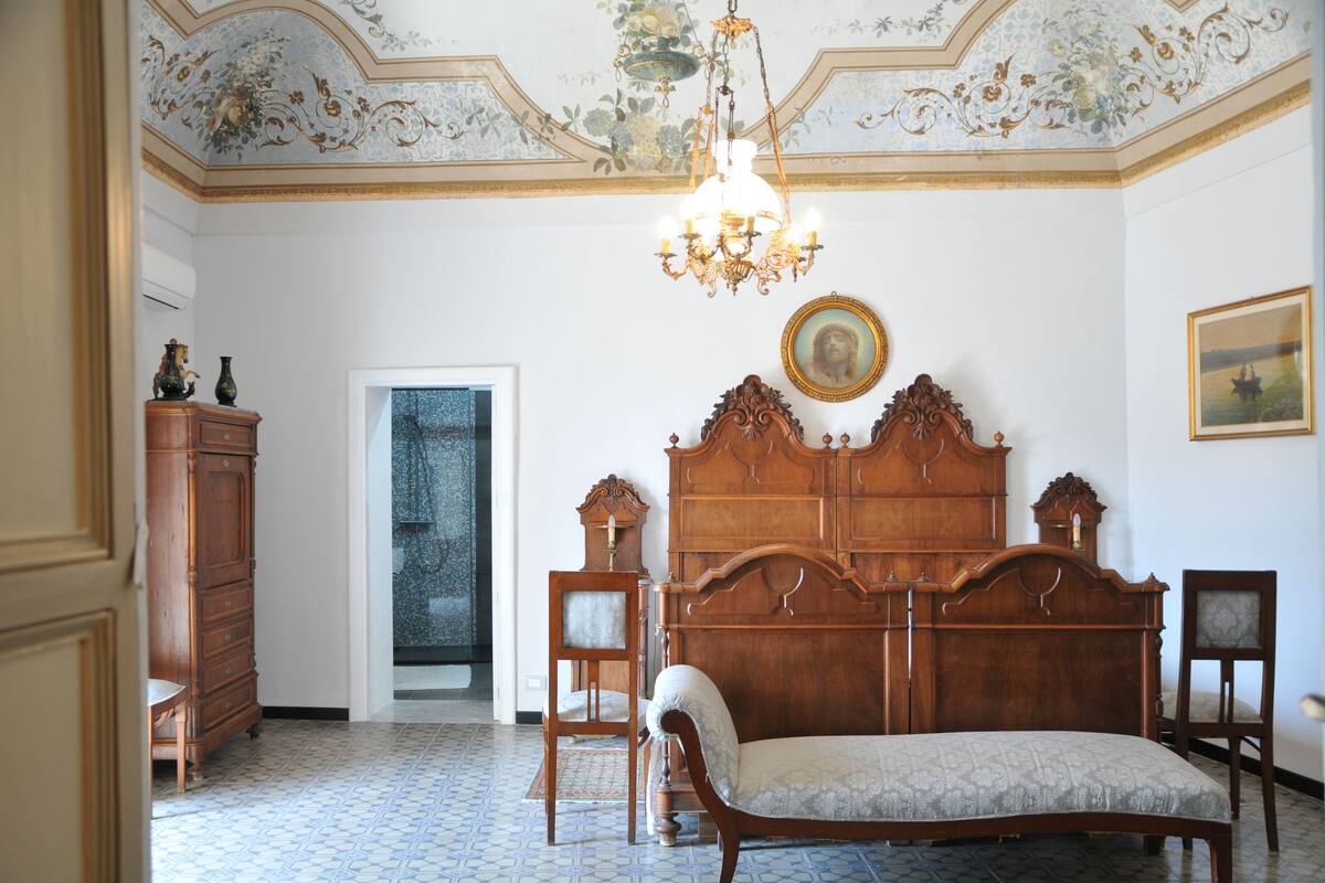 A bedroom with a wooden bed, a chandelier, a dresser, and a chair.