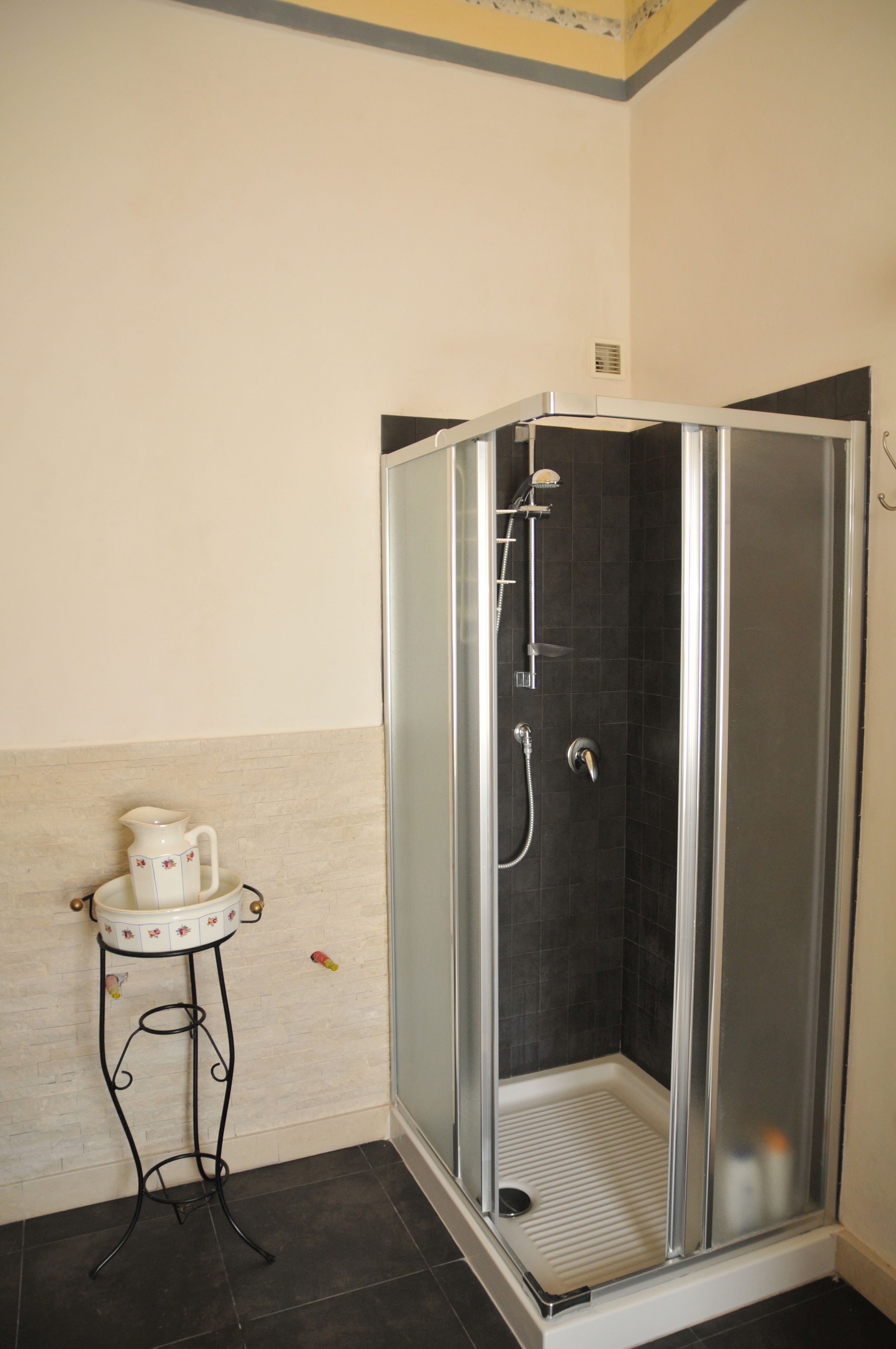 Un área de ducha con puerta de cristal, una mesita con jarrón, y suelo de baldosas.