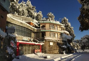 Un edificio con balcón y toldo rojo, rodeado de árboles cubiertos de nieve.
