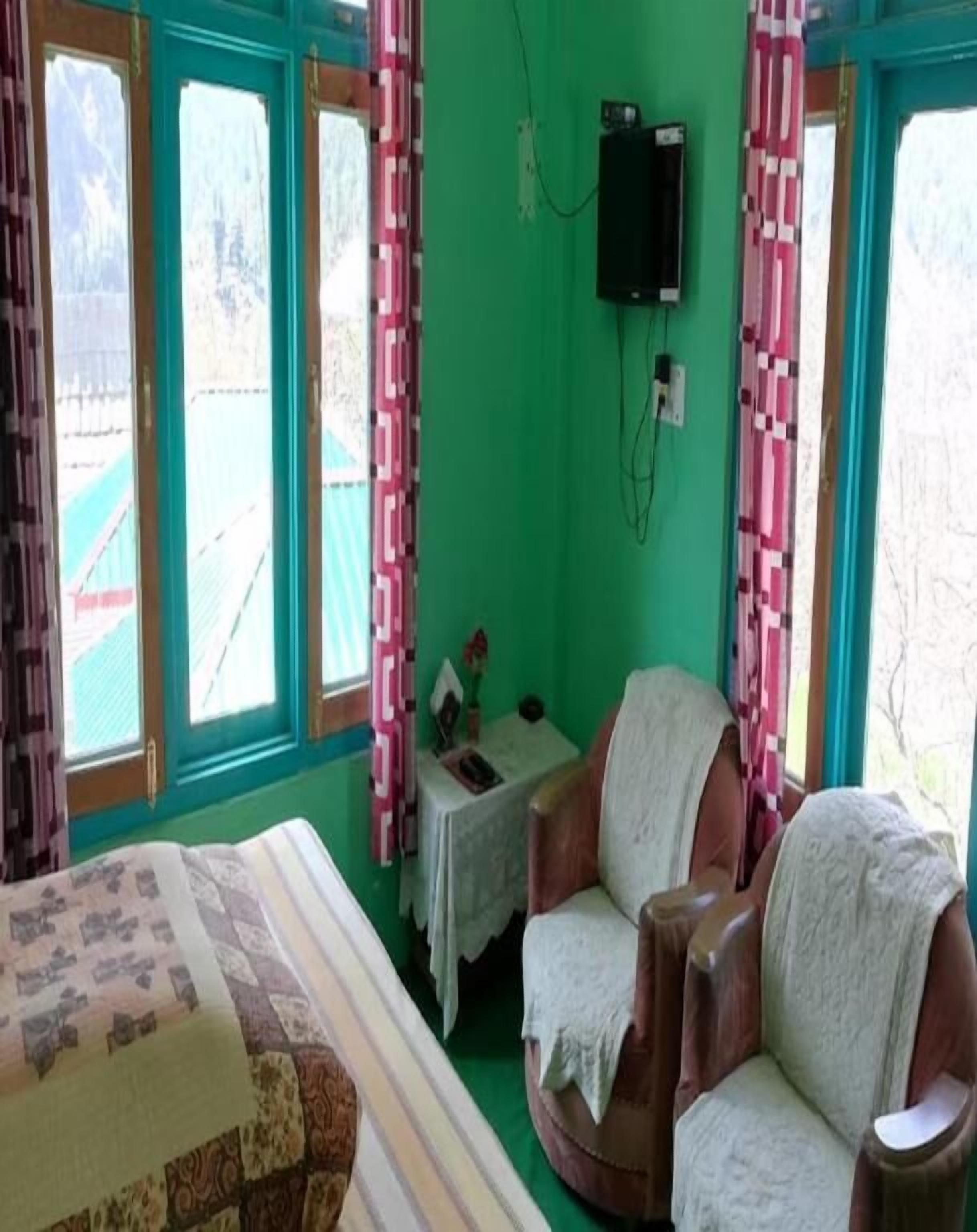 A room with a bed, two armchairs, a small table, and a television.