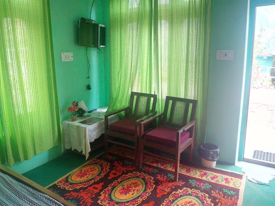 Una habitación con dos sillas de madera, una mesa pequeña con una flor y una cortina verde.