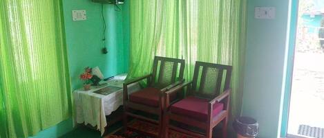 Una habitación con dos sillas de madera, una mesa pequeña con una flor y una cortina verde.