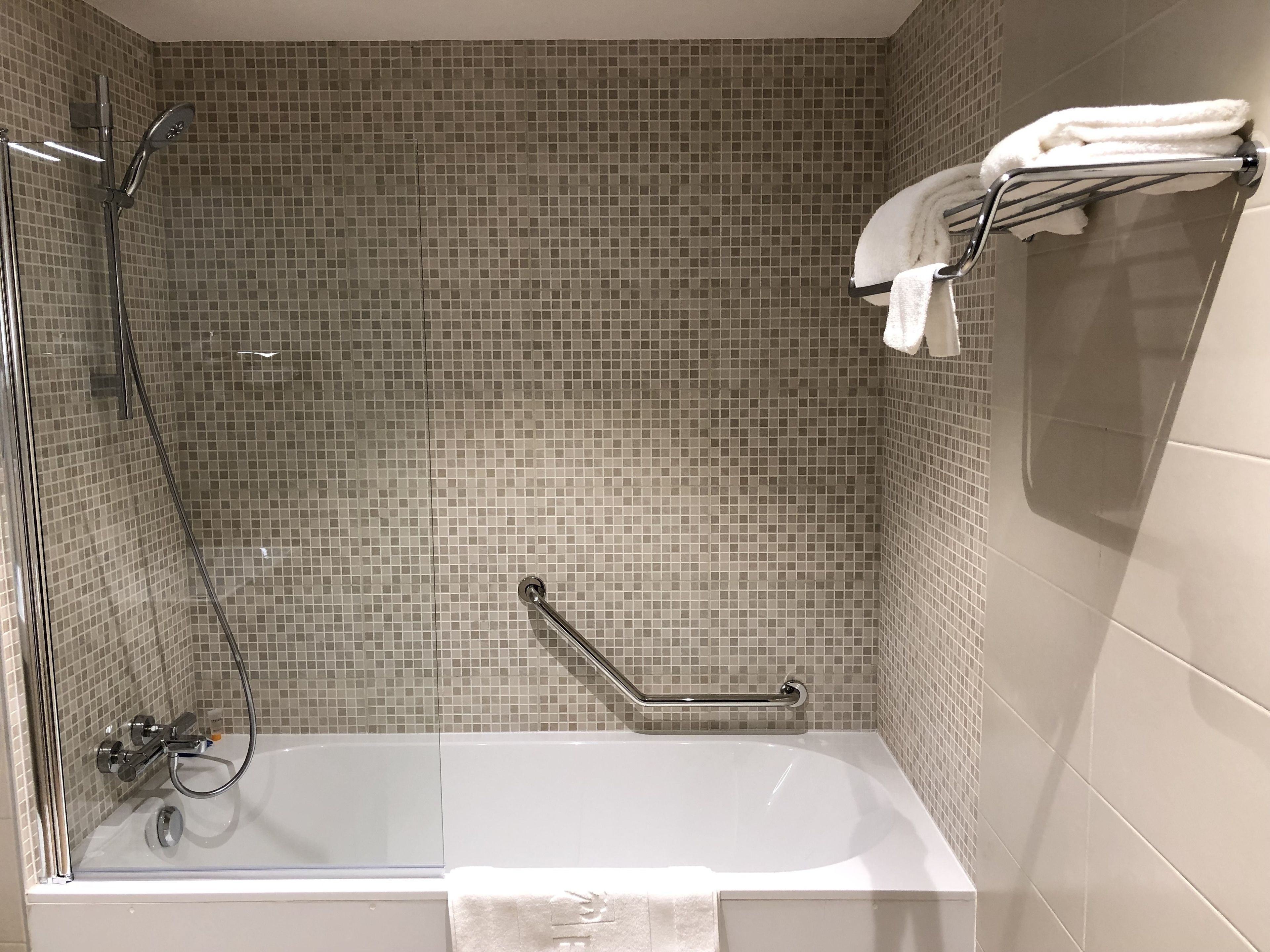 Um banheiro moderno com banheira de vidro, chuveiro com chuveiro manual e porta-toalhas com toalhas dobradas.