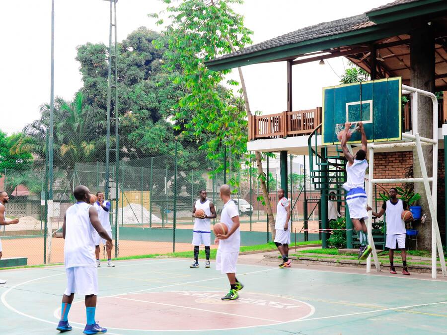 A basketball court with players in white uniforms, a basketball hoop, and a covered seating area.