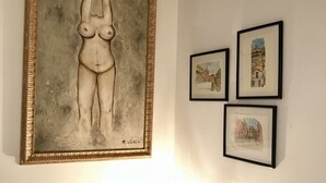 Ein Zimmer mit einem großen, abstrakten Gemälde an der Wand, einem kleinen Tisch mit einer Lampe und drei kleineren gerahmten Bildern.