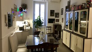 Eine moderne Küche mit Esstisch, Stühlen und einer Pendelleuchte. Ein Kühlschrank mit Glastüren und eine Pflanze sind in der Mitte platziert.