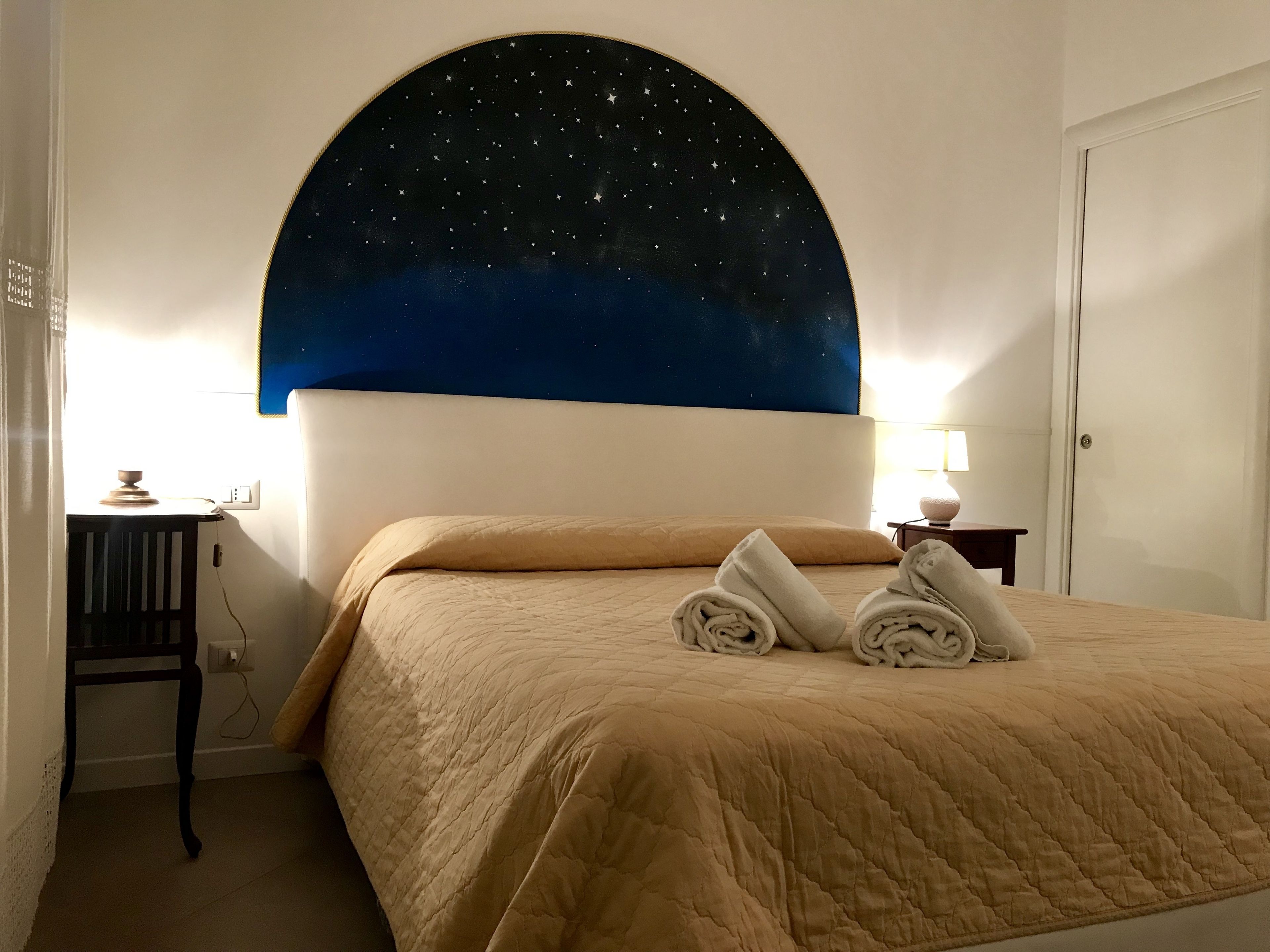 A hotel room with a bed, a night sky mural on the wall, a desk, and a lamp.